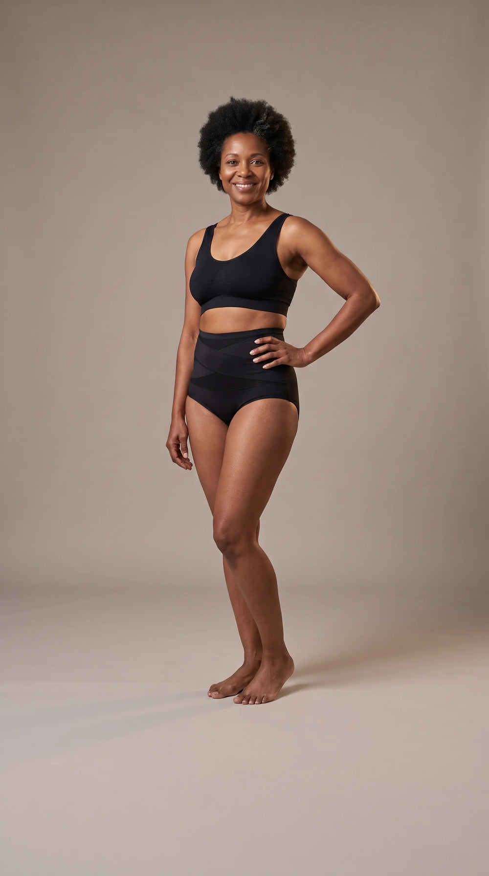 Black mom in her mid-forties wearing the black Snoothe 360° postpartum brief and a sports bralette in a photo studio